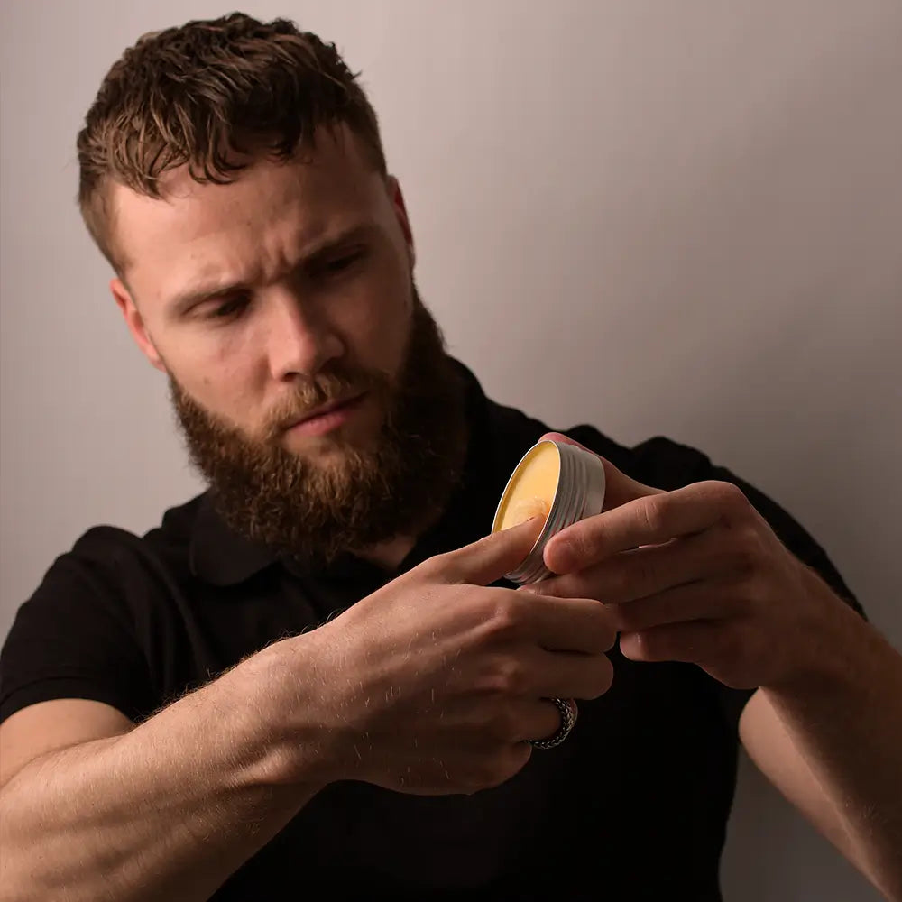 Een man die baardbalsem uit een potje baardbalsem schraapt.